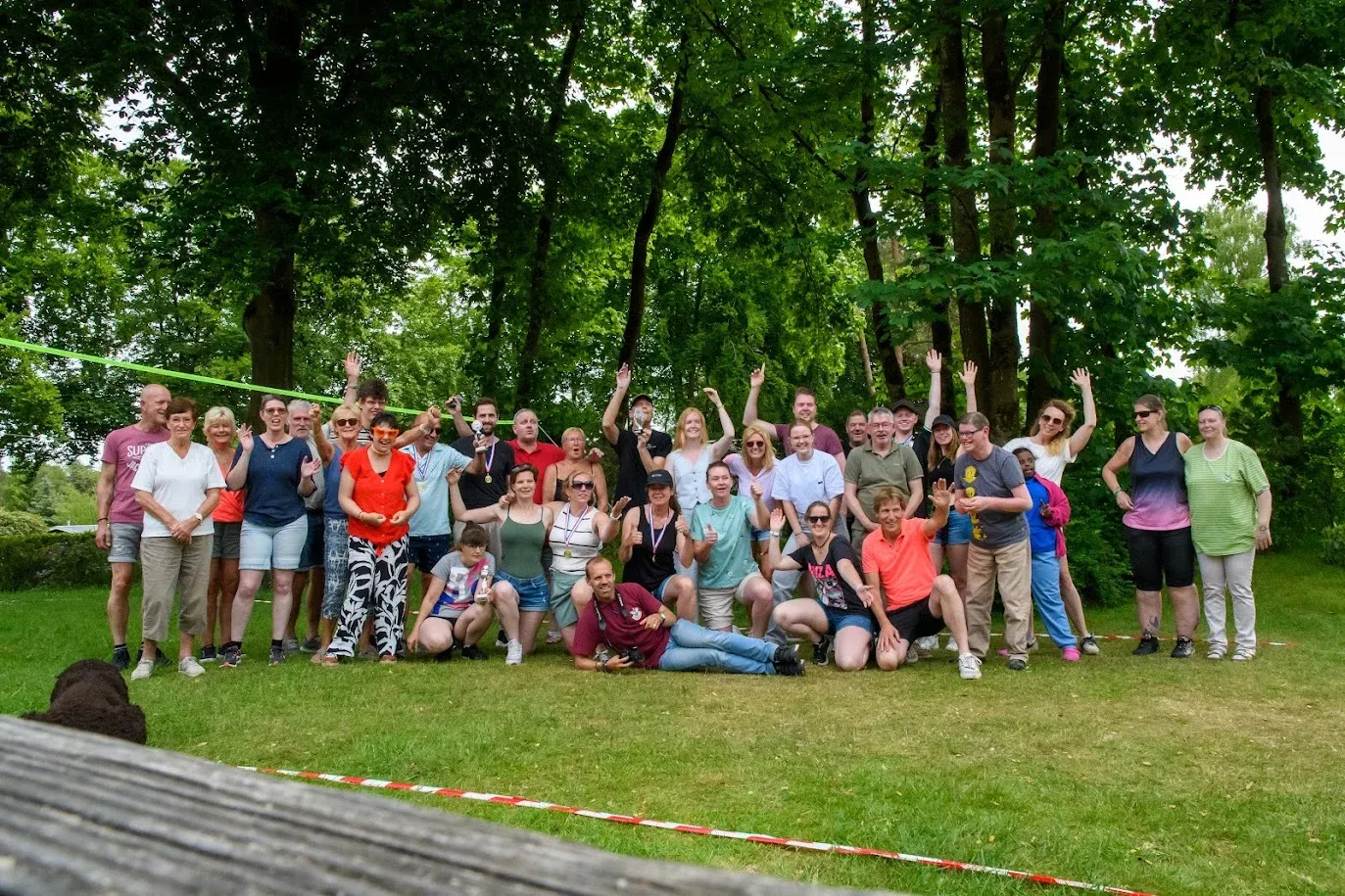 De hele groep ruiters en vrijwilligers poseert samen op het gras tussen de bomen op het kampeerterrein.