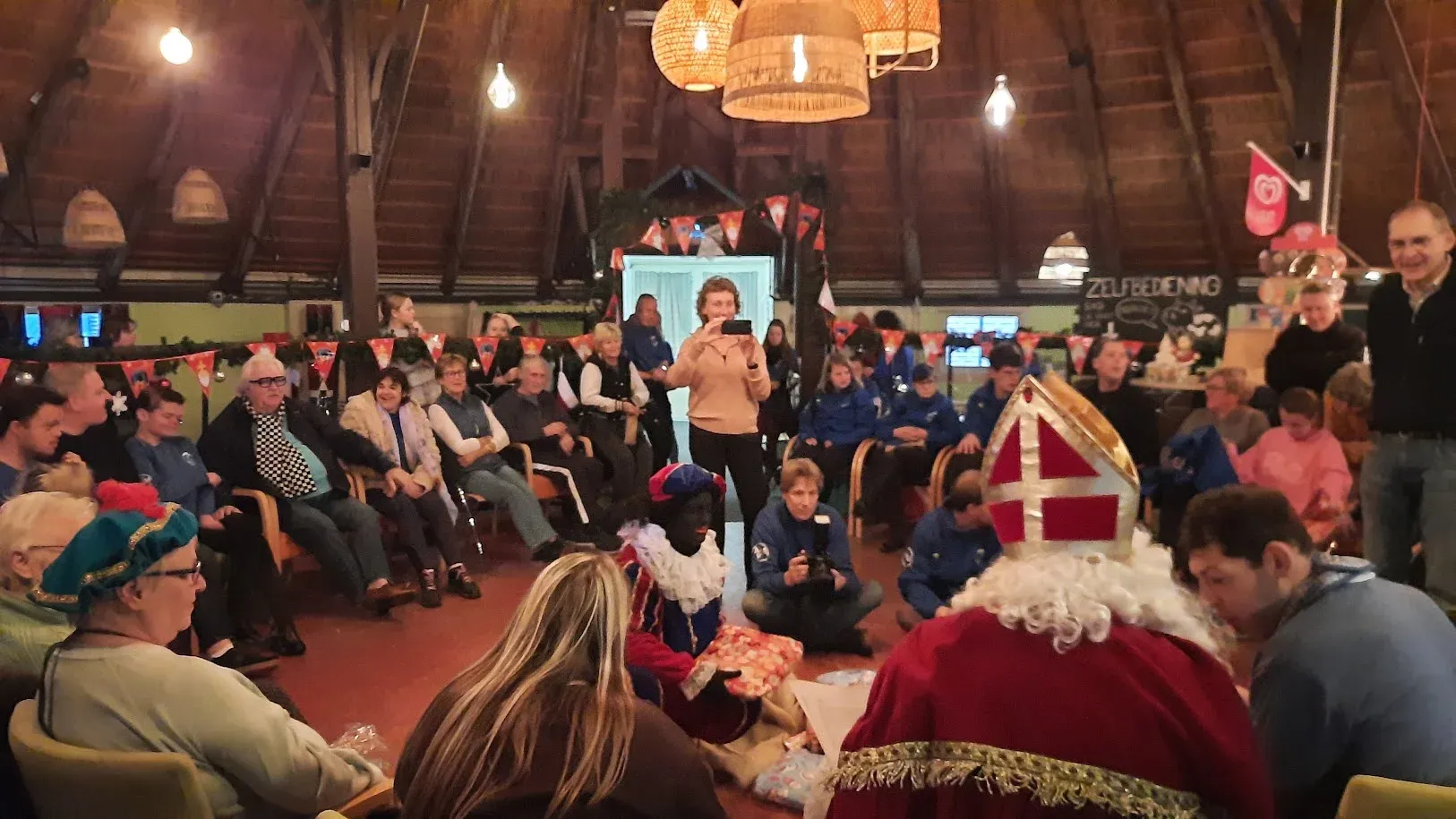 Sinterklaas deelt cadeaus uit in de feestelijk versierde Koestal, met ruiters, familie en vrijwilligers in een kring eromheen.